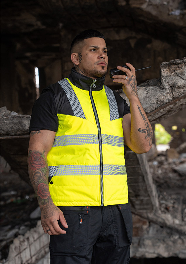 Erwachsener in signalgelbem Korntex-Softshell-Bodywarmer mit Reflexstreifen in einem industriellen Umfeld