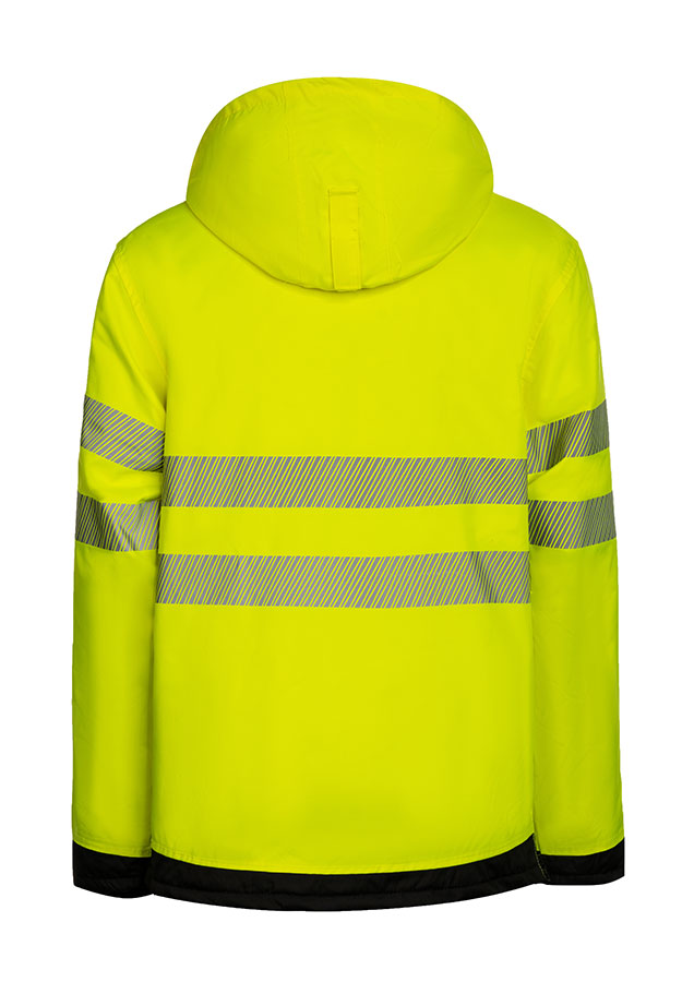 Erwachsener in signalgelbem Korntex-Parka mit schwarzer Brustpartie und Reflexstreifen in einem industriellen Umfeld