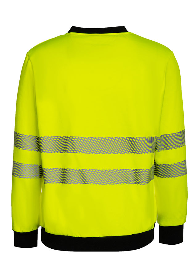 Erwachsener trägt ein gelbes Korntex-Sweatshirt mit schwarzer Brustpartie in einem industriellen Umfeld