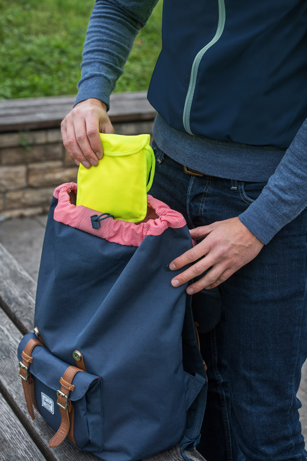 Erwachsener verstaut gelbe Warnweste in einem blauen Rucksack