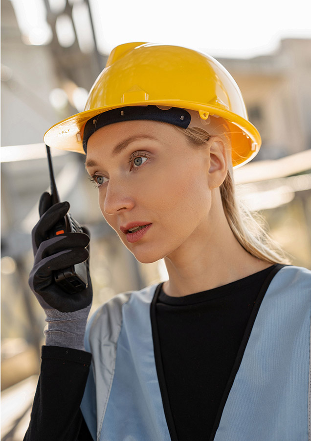 Blonde Frau mit gelbem Helm und Walkie-Talkie.