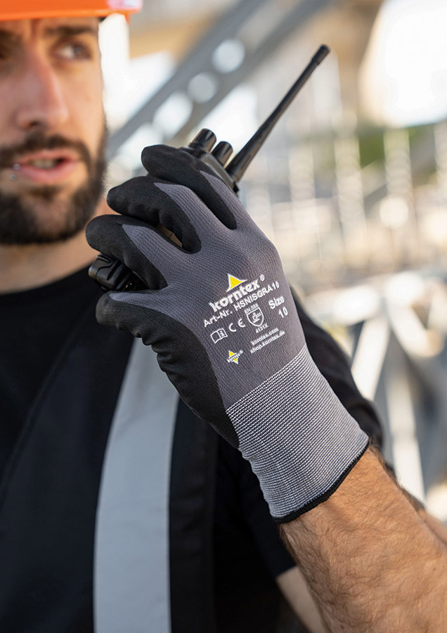 Ein Mann mit grau-schwarzen Korntex-Handschuhen hält ein Walkie-Talkie