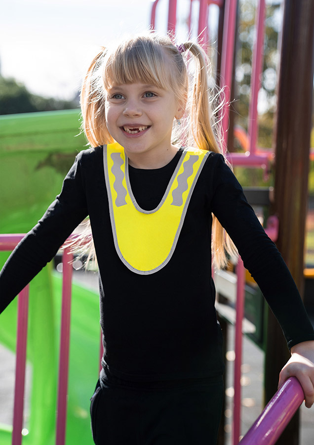 Ein Kind in einem gelbfarbenen Korntex Multifunktionskragen mit Reflexstreifen steht in einem Park