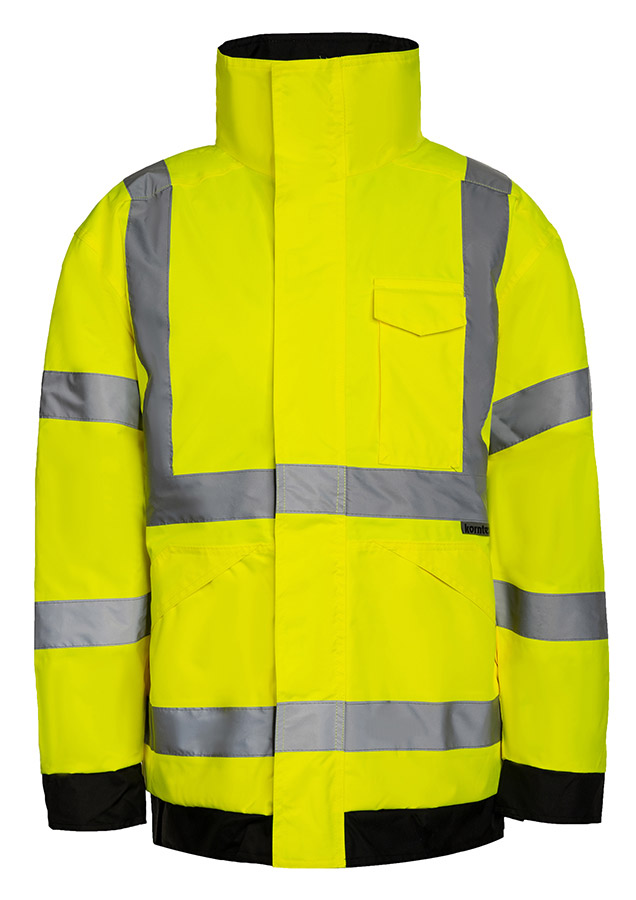 Erwachsener Bauarbeiter in gelber Korntex Hochsichtbarkeits-Regenjacke und gelbem Schutzhelm trägt eine Schaufel auf einer Baustelle.