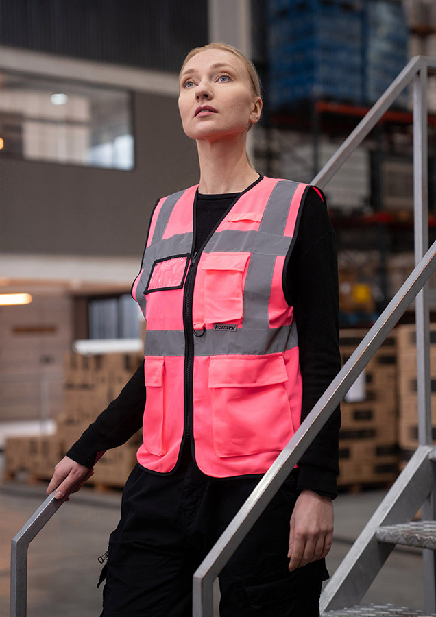 Eine Frau trägt eine pinkfarbene Korntex-Sicherheitsweste mit Reflexstreifen in einem Lagerhaus