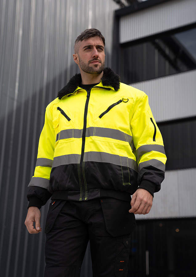 Ein Mann in einer signalgelb-schwarzen Korntex-Pilotenjacke steht vor einem Gebäude