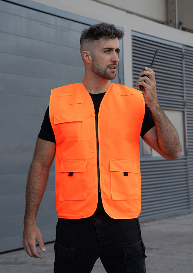 Erwachsener in orangefarbener, gefütterter Korntex-Arbeitsweste mit Taschen vor einem Gebäude