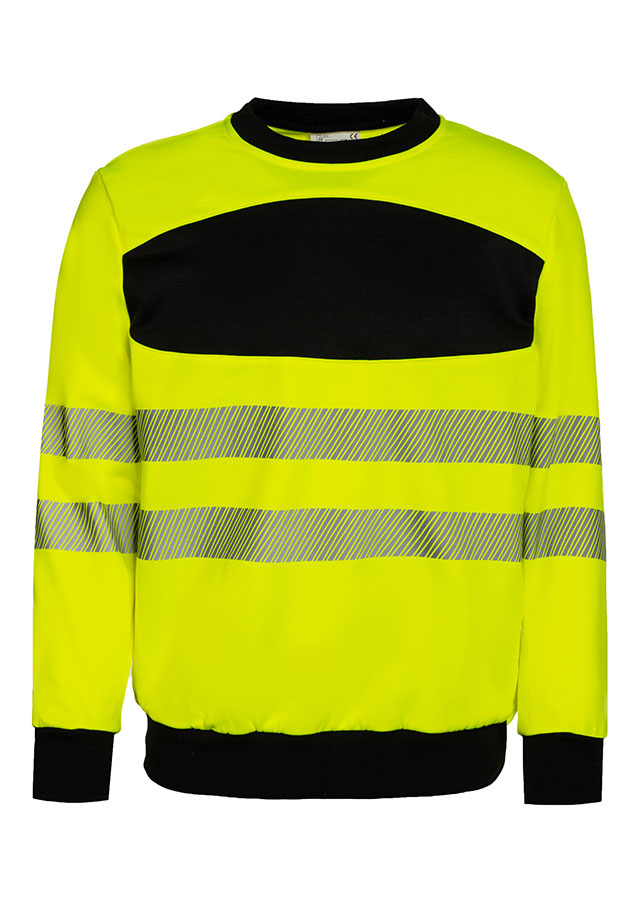 Erwachsener trägt ein gelbes Korntex-Sweatshirt mit schwarzer Brustpartie in einem industriellen Umfeld