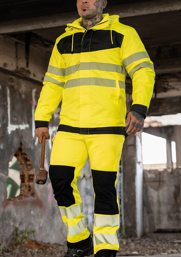 Erwachsener trägt unter anderem eine signalgelbe Korntex-Hose mit schwarzen Partien in einem industriellen Umfeld
